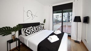 Habitación de hotel moderna con una cama grande, un cojín blanco y negro estampado, una lámpara de pie negra y vistas a la ciudad desde un balcón.