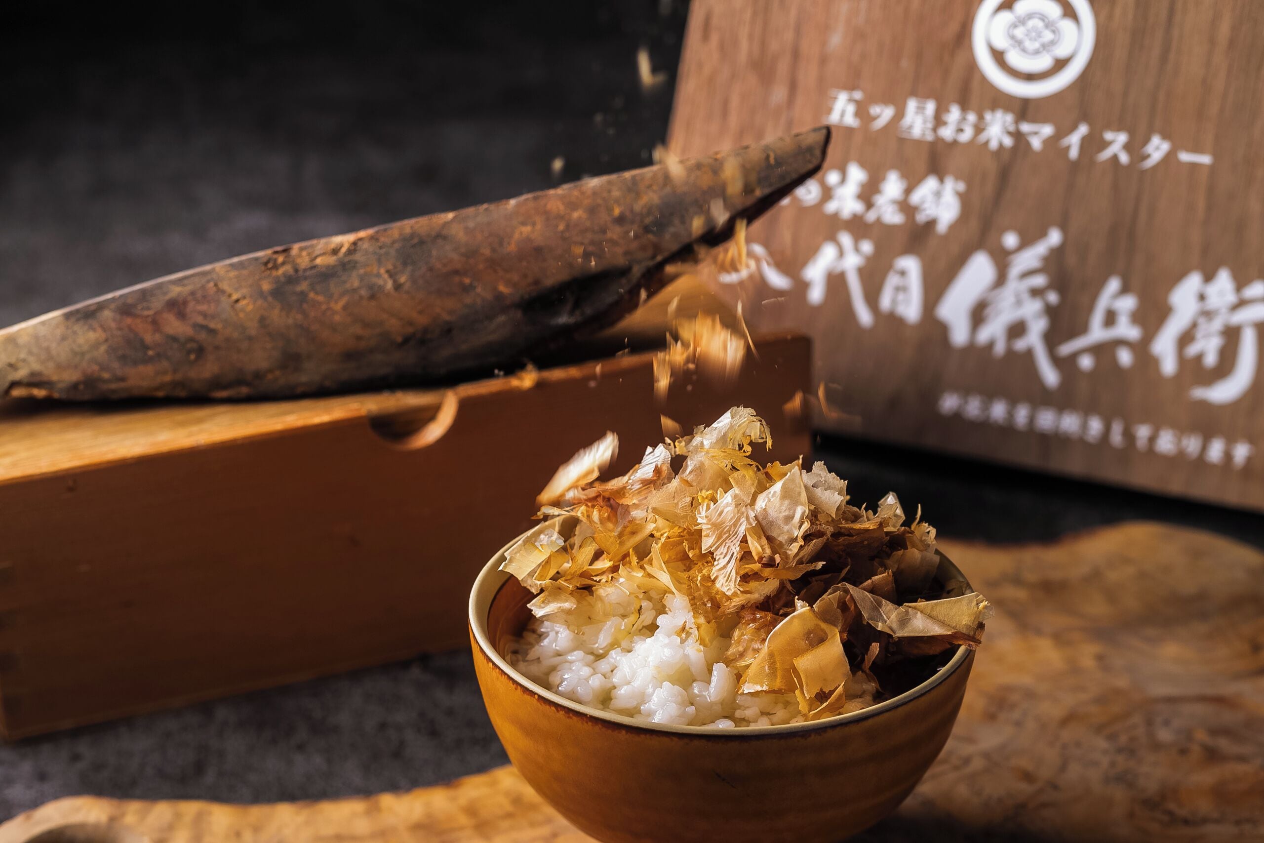 A wooden bowl with rice and shredded seaweed, a wooden cutting board, and a knife.
