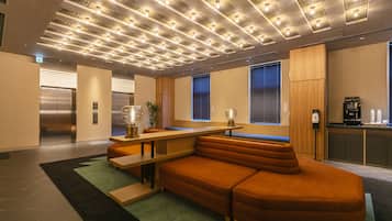 A modern hotel lobby with a sectional sofa, a long table, and a kitchen area.