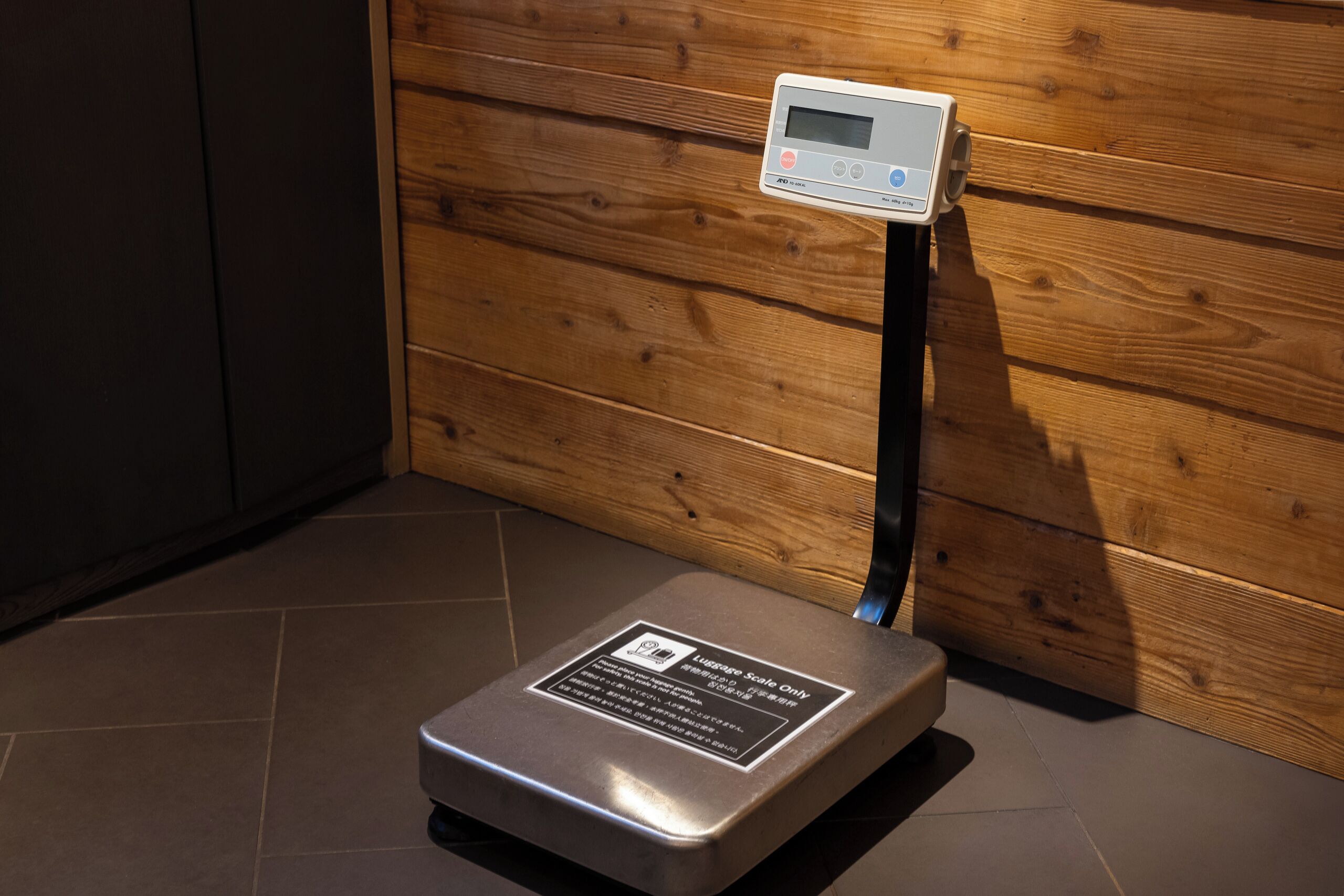 A weighing scale with a label, a digital display, and a wooden wall in the background.
