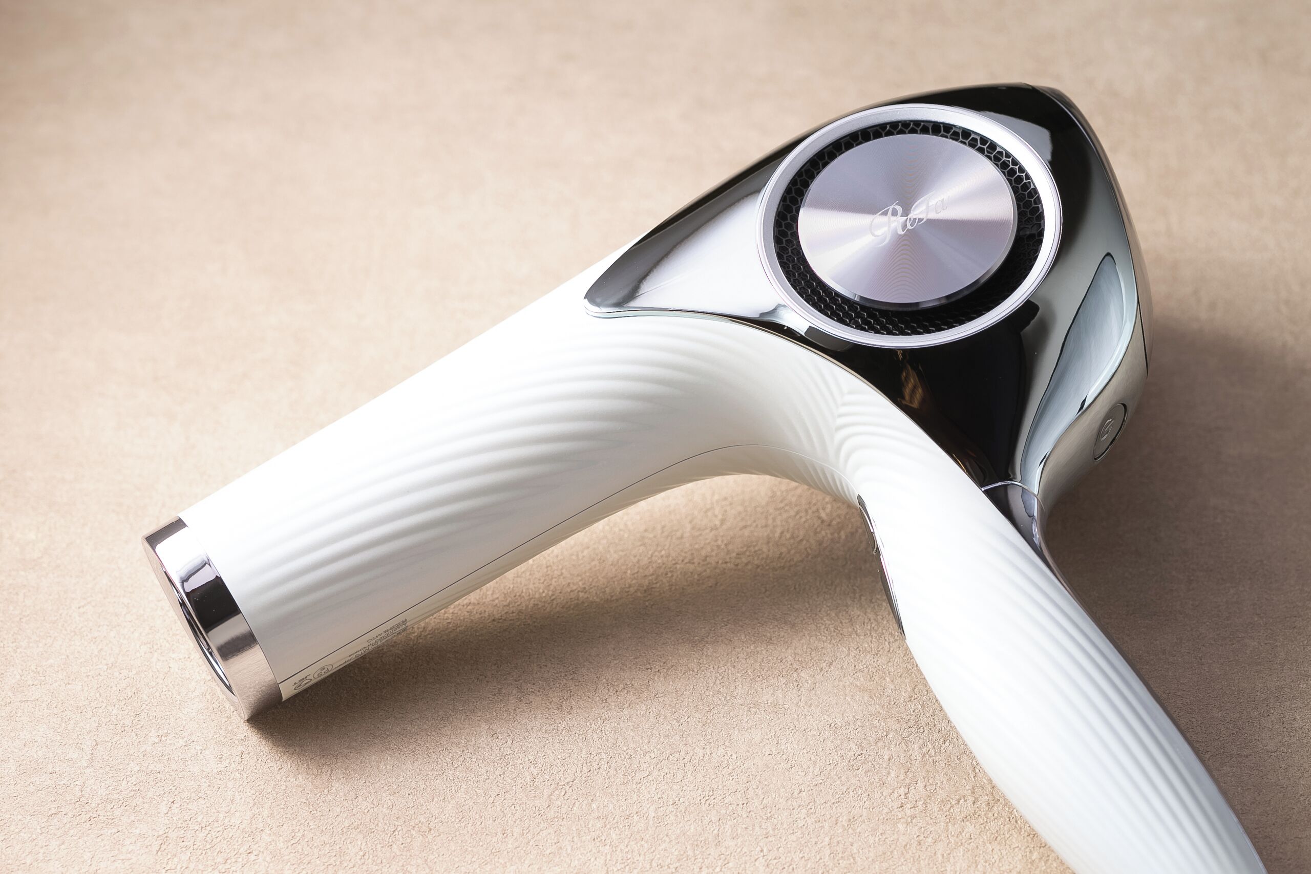 A white and black hairdryer with a ribbed handle and a circular control panel.