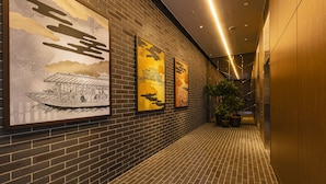 A hallway with brick walls and tiled flooring, featuring three framed artworks depicting traditional scenes. - Hotel Forza Osaka Namba Dotonbori (Osaka)