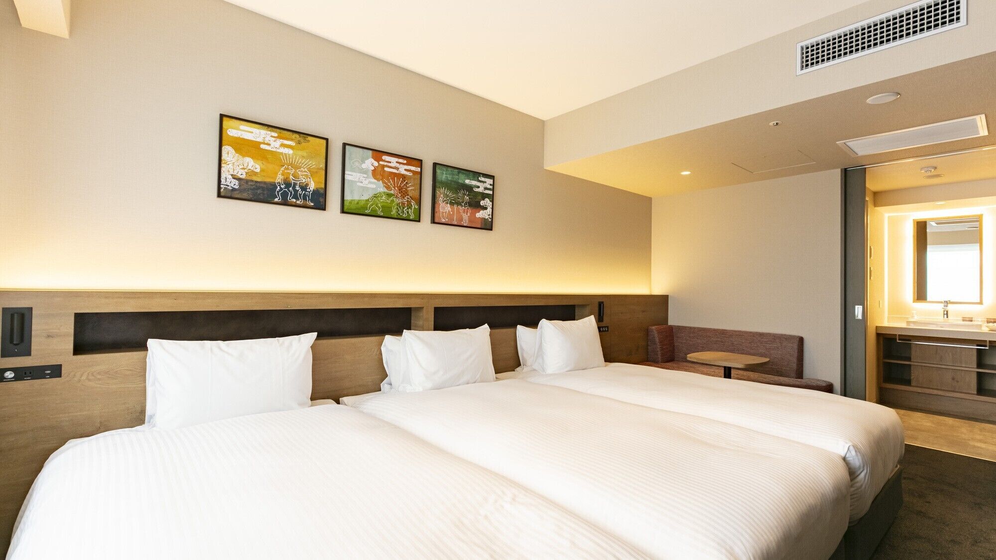 A hotel room with a large bed, a small seating area, and artwork on the wall.
