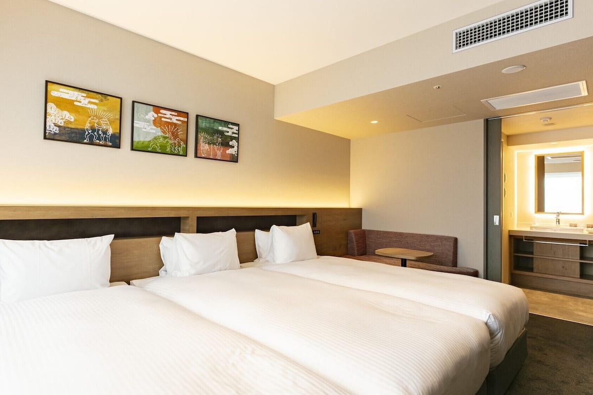 Una habitación de hotel con una cama grande, una zona de estar pequeña y obras de arte en la pared.