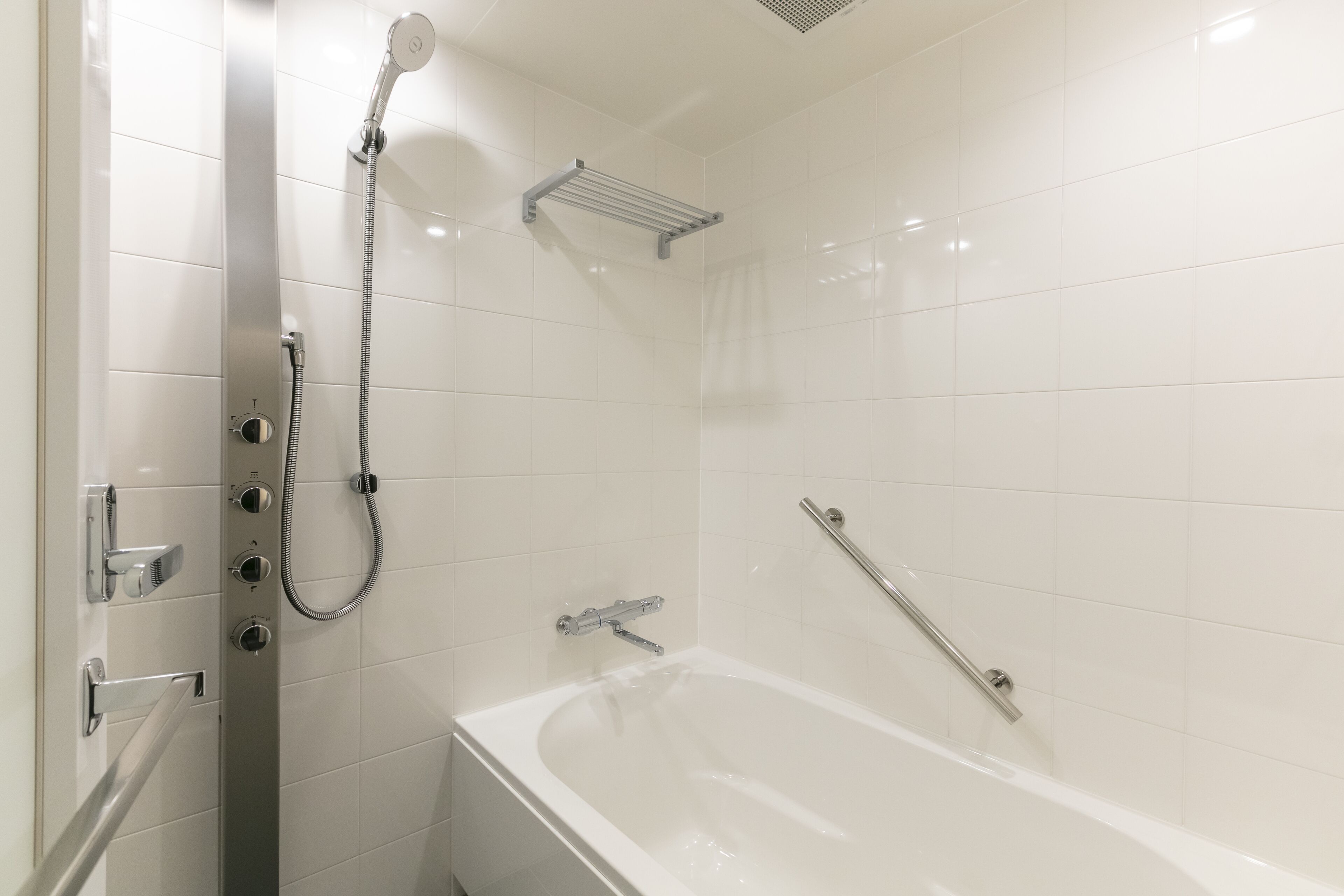 A modern bathroom with a bathtub, a shower with a handheld showerhead, and a grab bar for safety.