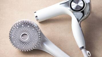 A hair dryer and brush with a metallic and white design, placed on a beige surface.