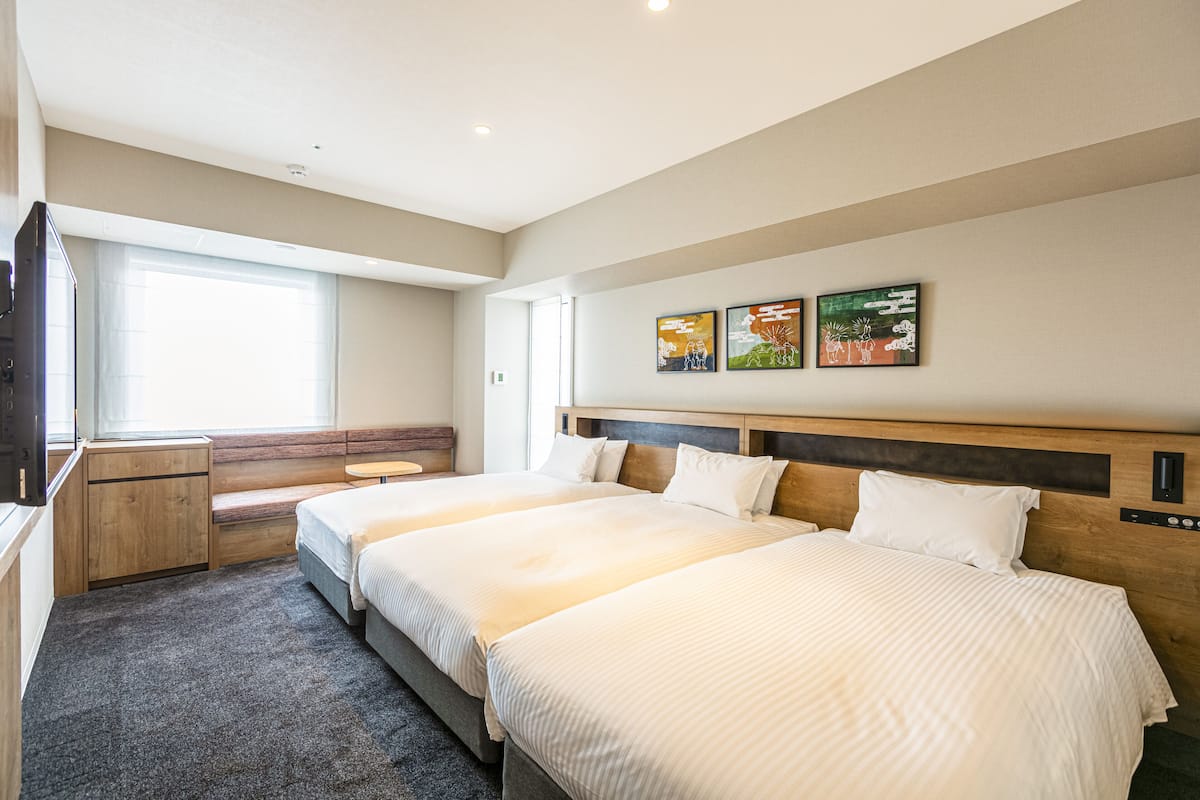 Habitación de hotel con dos camas, un escritorio, un banco y obras de arte en la pared.