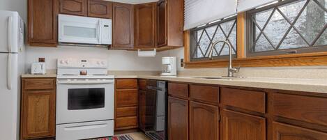 A kitchen with wooden cabinets, a white stove, a microwave, and a dishwasher.