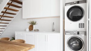 A modern kitchen with white cabinets, a wooden dining table, and a built-in washer and dryer. - Crystal Pacific Palm Beach (Palm Beach)