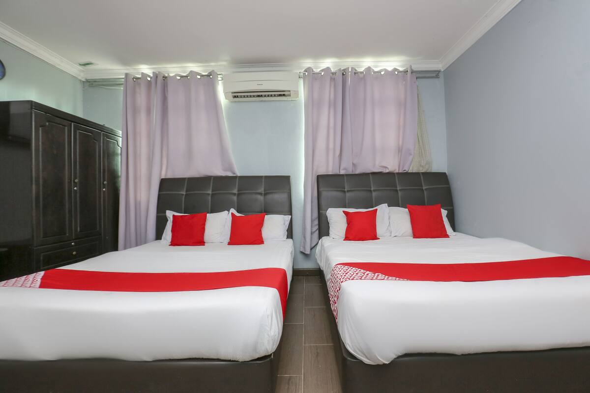 Habitación de hotel con dos camas, cada una con ropa de cama blanca y detalles rojos, cabecero oscuro y armario.