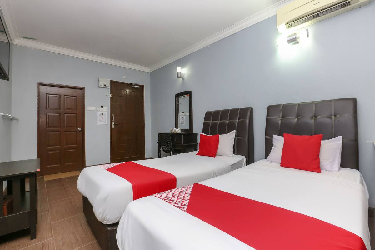 Una habitación de hotel con dos camas, un escritorio, un armario y aire acondicionado.