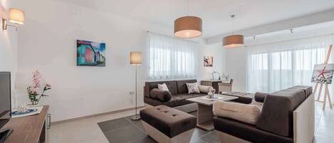 A modern living room with a sofa, ottoman, and coffee table, a painting on the wall, and a lamp.