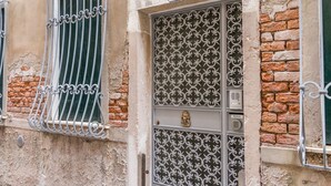 A building facade with a metal gate, a window with a metal grille, and a door with a numeric plaque.