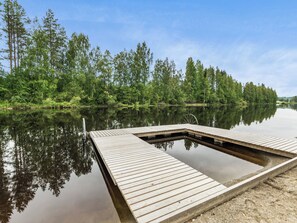 Une jetée en bois s’étendant sur un lac paisible, entouré d’une forêt dense.