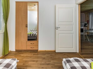 Une pièce avec une armoire en bois, un lit recouvert d’une couette à carreaux et une porte donnant sur une autre pièce.