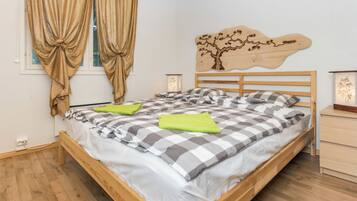 A bedroom with a wooden bed, checkered bedding, a nightstand, a wall-mounted lamp, and a window with curtains.
