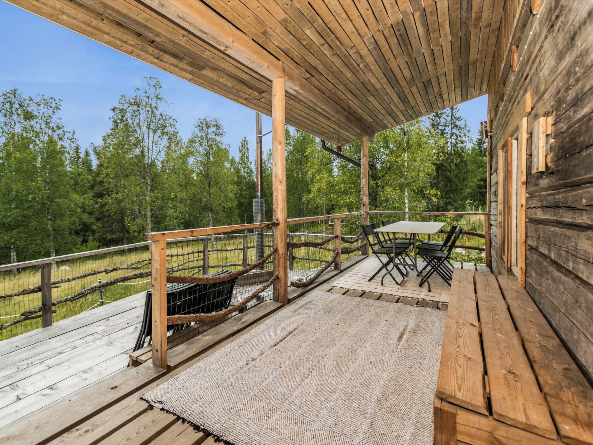 A wooden deck with a table and chairs, surrounded by a wooden railing and a view of trees.