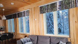 A cozy cabin interior with a wooden ceiling, large windows with forest views, a gray sofa, and a dining area with chairs. - Vacation home Koivu by Interhome (Sonkajärvi)
