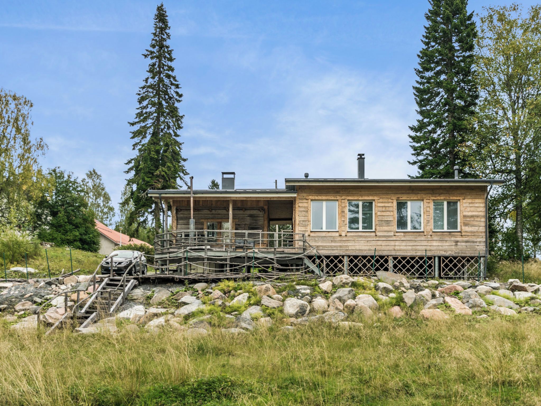 A wooden cabin with a deck, surrounded by rocks and trees.