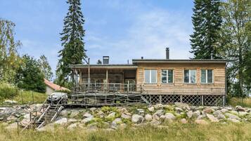 A wooden cabin with a deck, surrounded by rocks and trees.