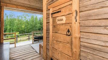A wooden door labeled 'SAUNA' with a metal handle and a metal latch, leading to an outdoor deck with a railing.