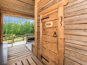 Une porte en bois portant l’inscription « SAUNA », dotée d’une poignée et d’un loquet en métal, qui donne sur une terrasse extérieure avec une rambarde.
