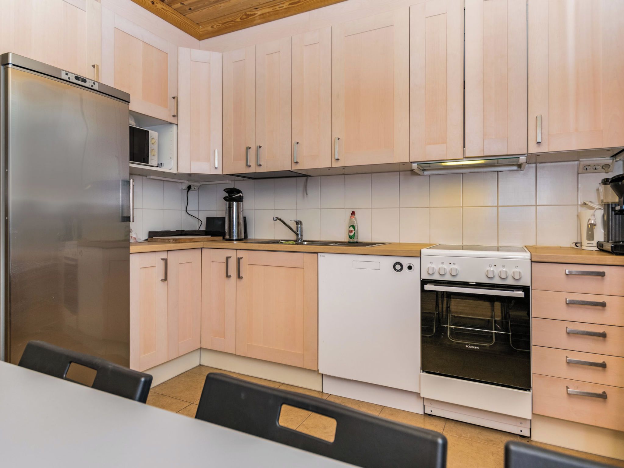 A modern kitchen with light wood cabinets, stainless steel appliances, and a wooden countertop.