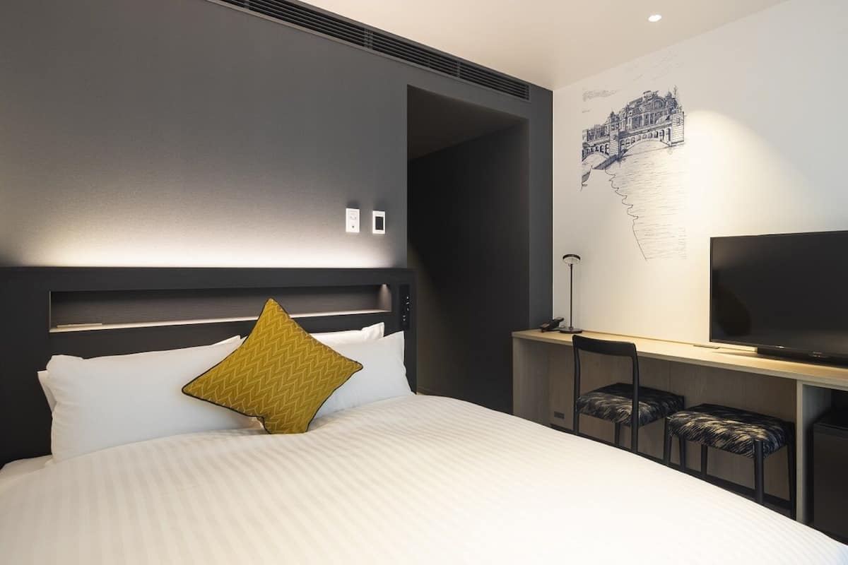 Ein modernes Hotelzimmer mit einem großen Bett, einem Flachbildfernseher, einem Schreibtisch mit Stuhl und einem Wandbild.
