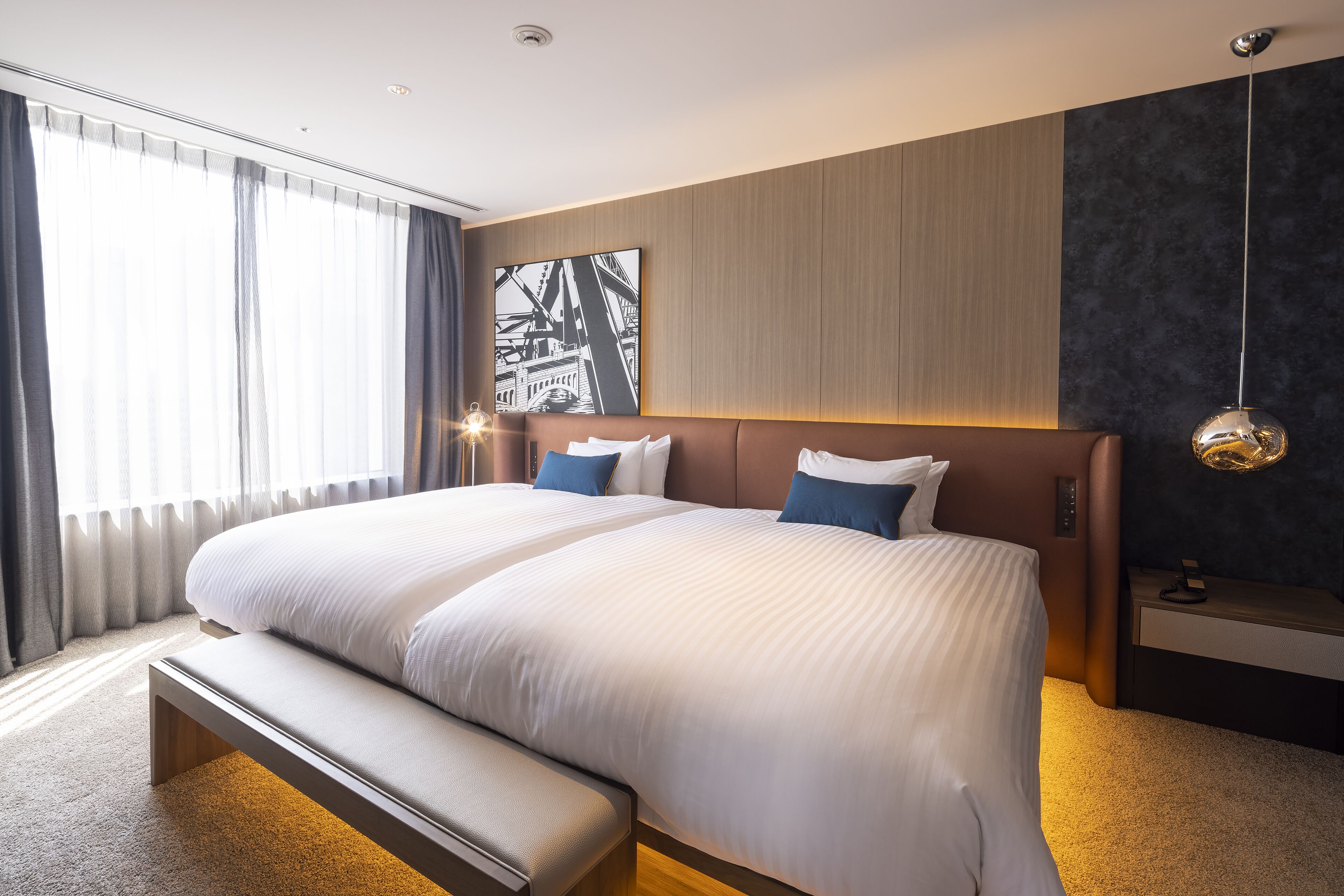 Una camera d'albergo moderna con un ampio letto, una panca e un dipinto con vista sulla città.