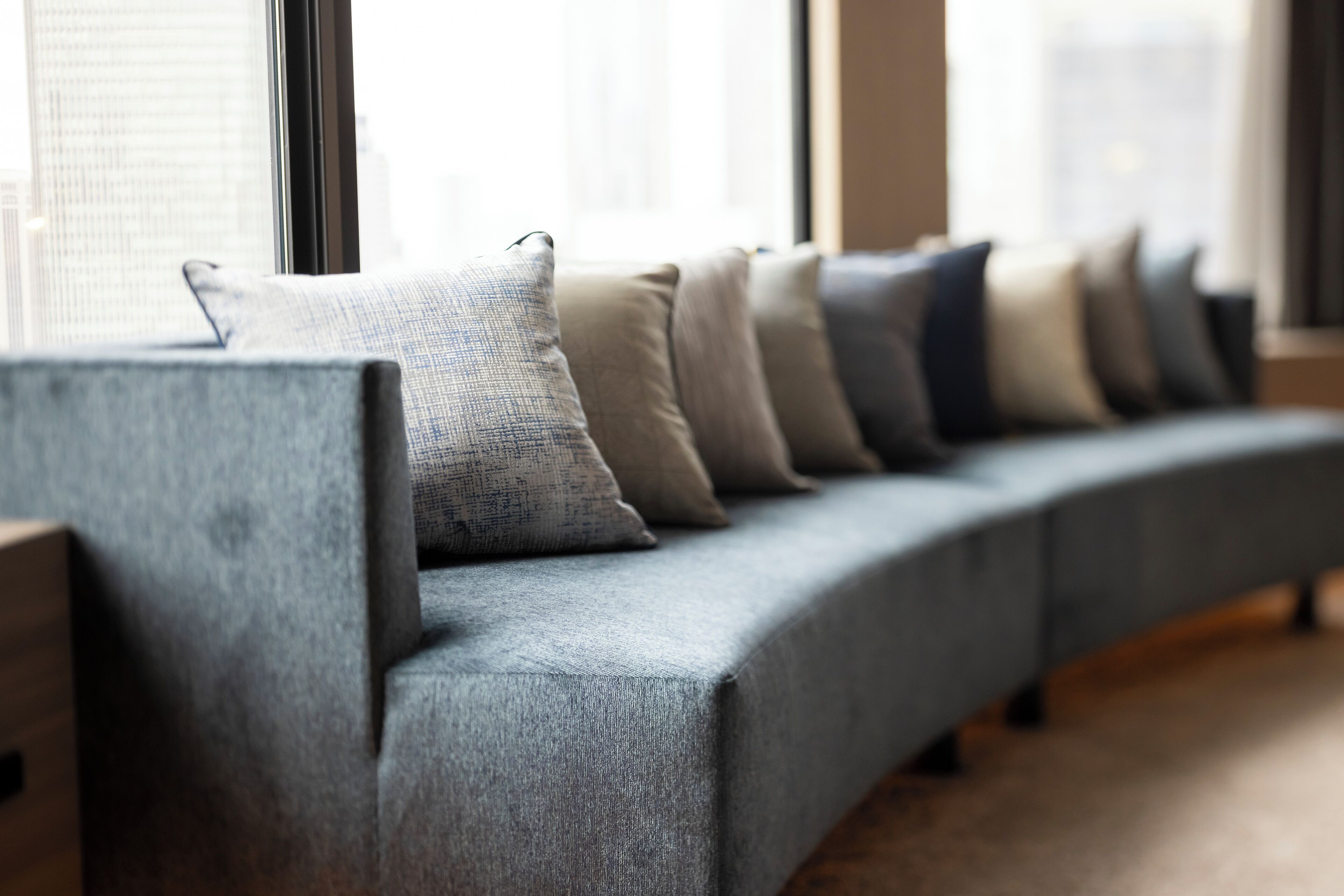 A modern sofa with multiple cushions in a well-lit room with large windows.