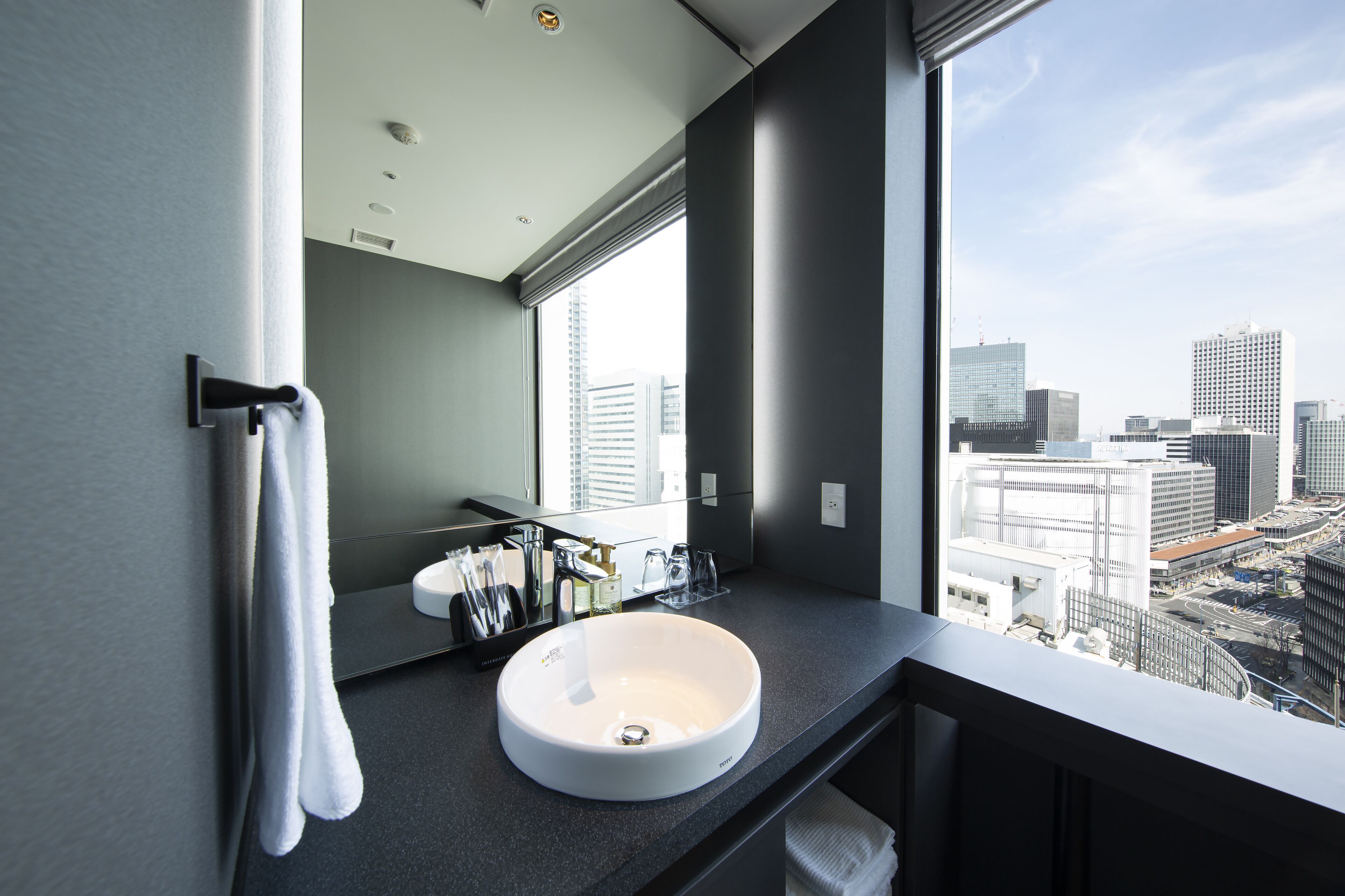 A modern bathroom with a large window, a white sink, and a towel rack.