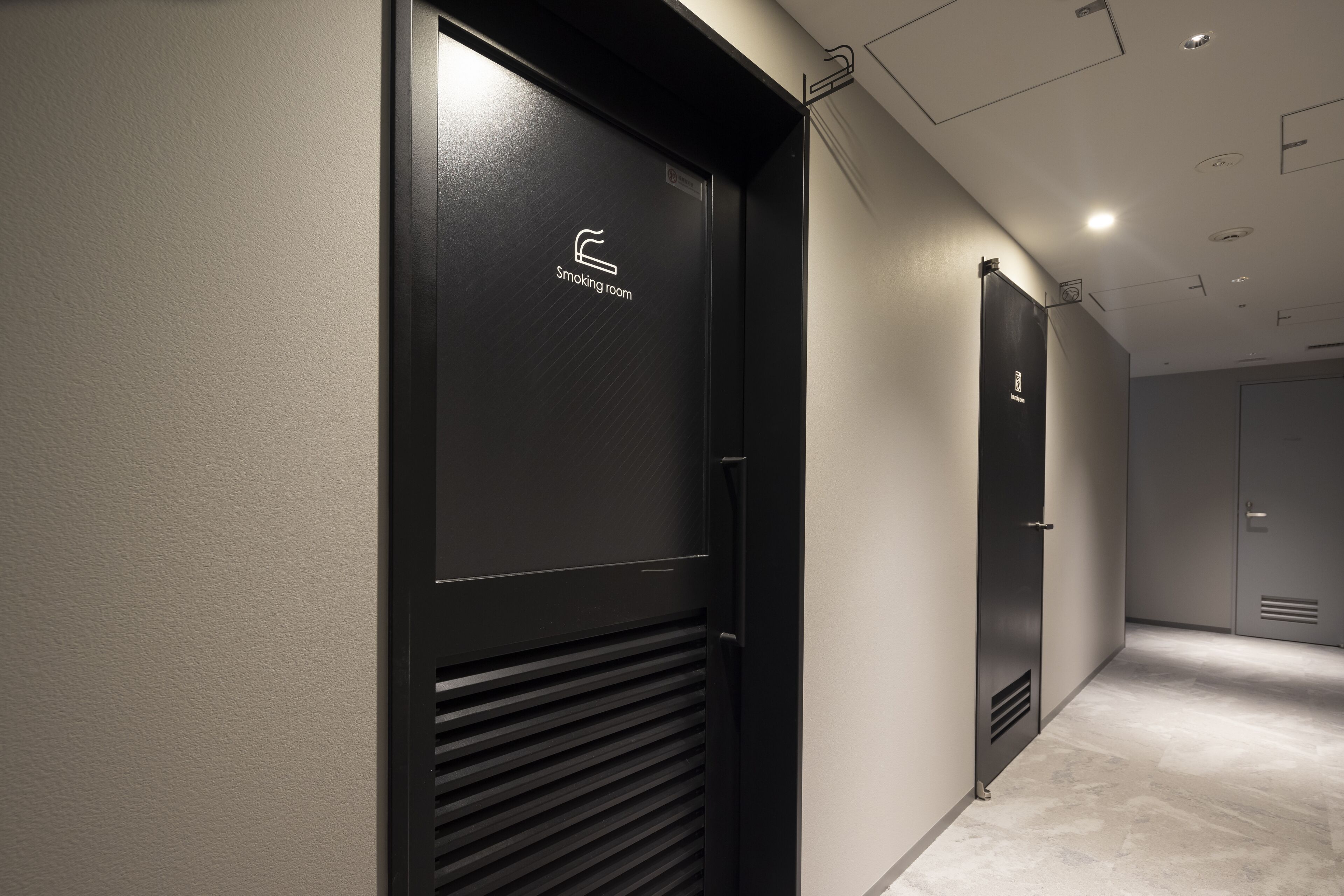 A hallway with a smoking room sign on a door, a vent, and a light fixture on the ceiling.