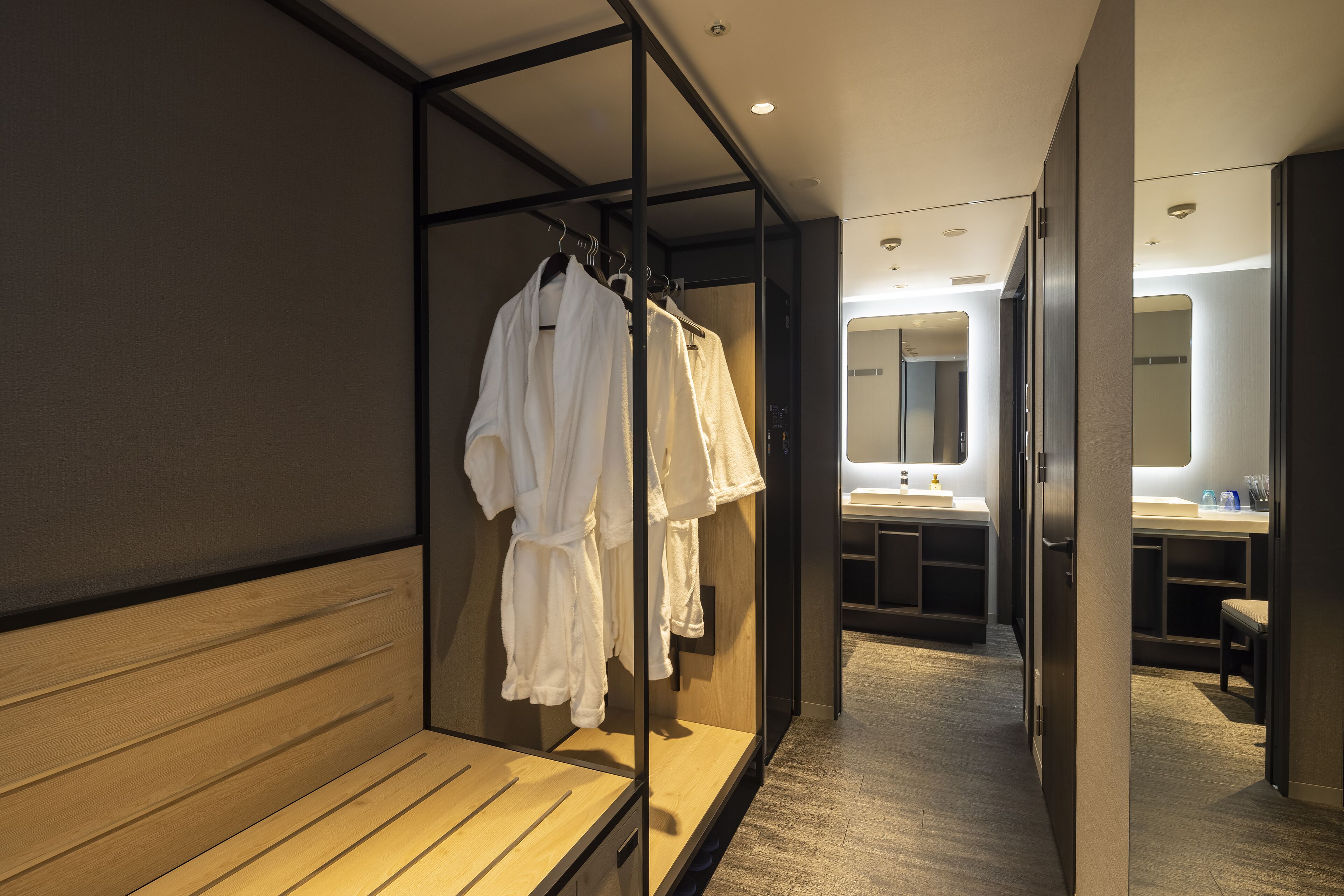 A hotel corridor with a wooden bench, a mirror, and a rack of white robes.