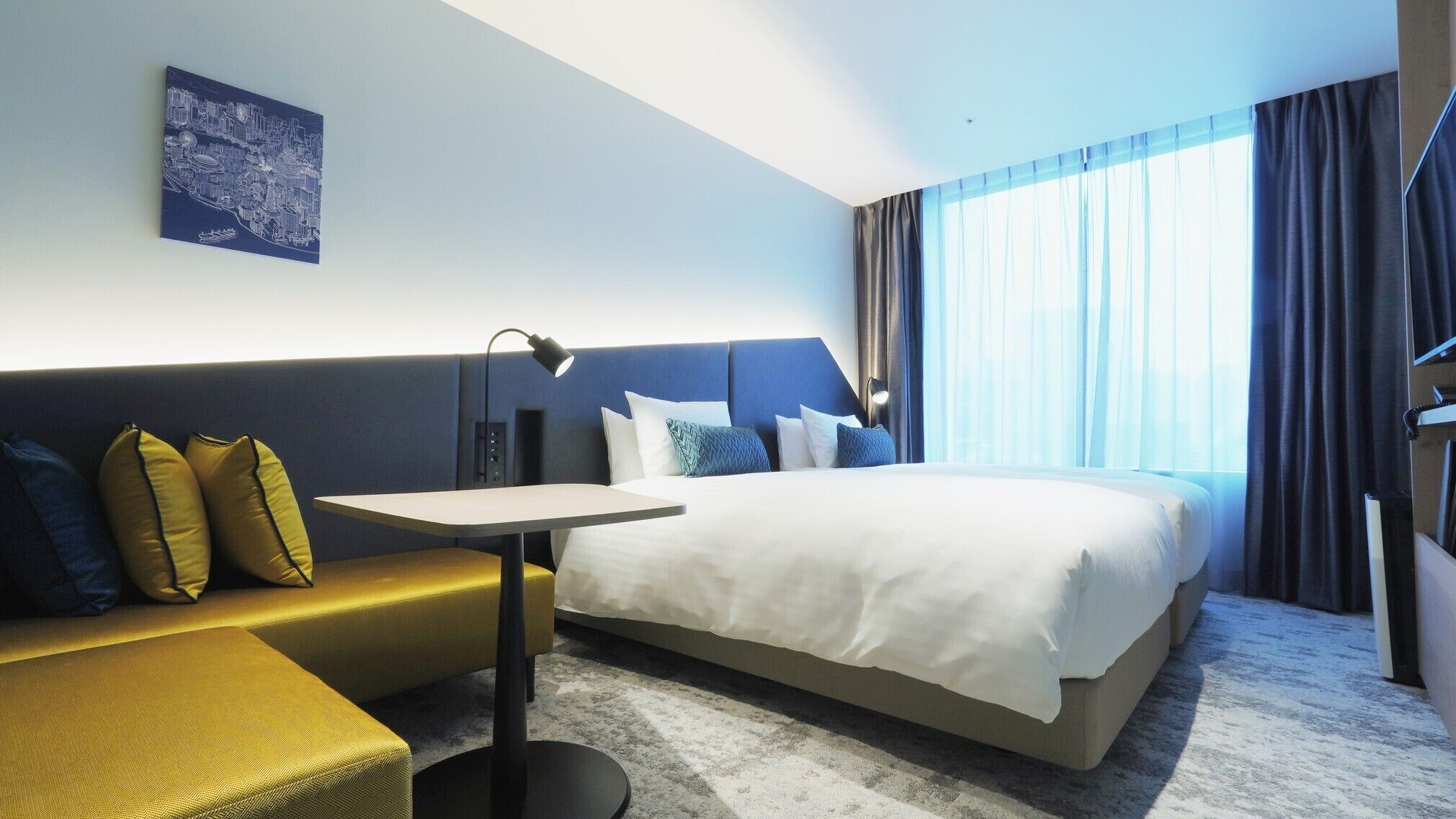 Ein Hotelzimmer mit einem Bett, einem Schreibtisch, einer Couch und einem großen Fenster mit Vorhängen.