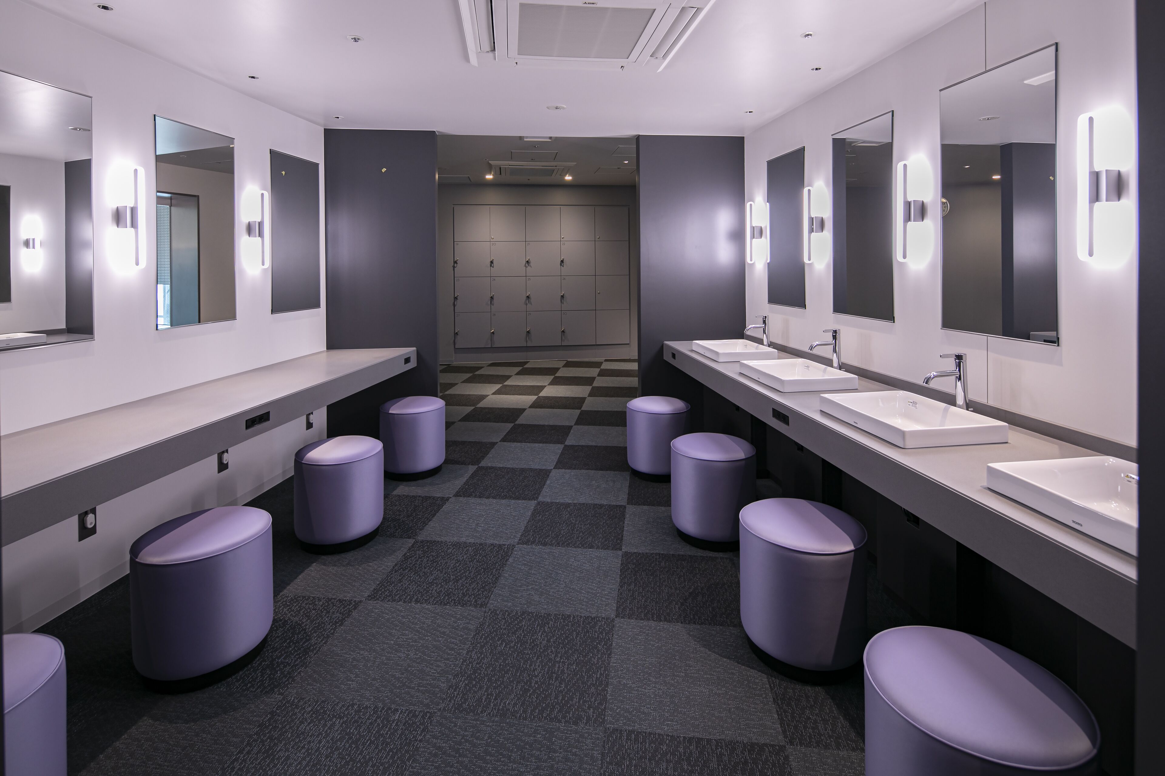 A modern bathroom with multiple sinks, mirrors, and purple stools.