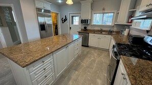 Une cuisine dotée de plans de travail en granit, de meubles blancs, d’appareils électroménagers en acier inoxydable et d’une cuisinière à gaz.