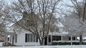 Une maison à deux étages, avec une clôture en bois peinte en blanc, un sol recouvert de neige et des arbres sans feuilles.