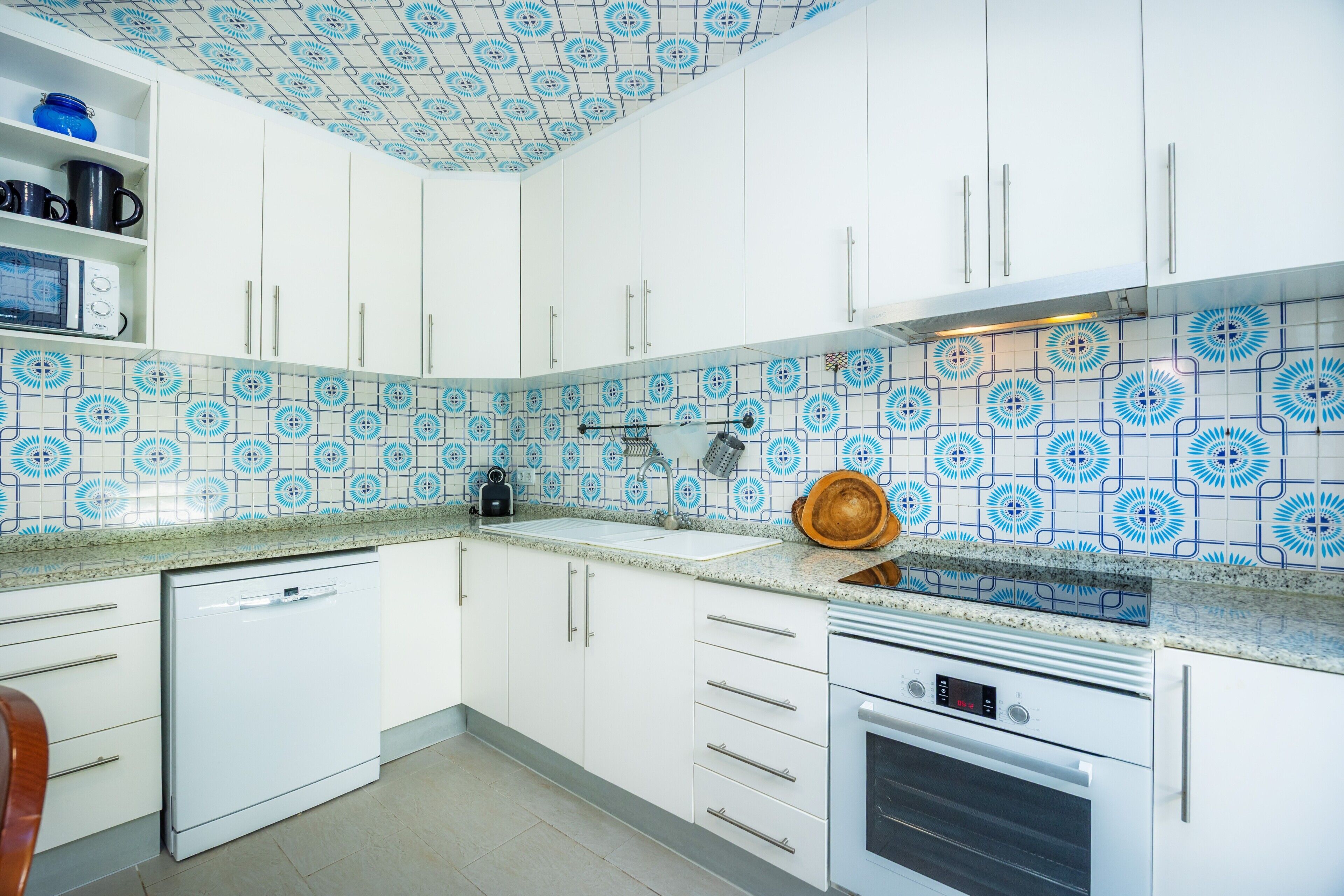 A kitchen with white cabinets, a microwave, a stove, and blue patterned tiles.