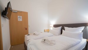 A hotel room with a neatly made bed, a wooden door, and a television mounted on the wall. - Double room economy - lodging house oystercatcher (Norderney)