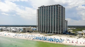 Ein Hochhaus-Hotel mit mehreren Balkonen, ein Strand mit zahlreichen Sonnenschirmen und freiem Blick auf den Ozean.