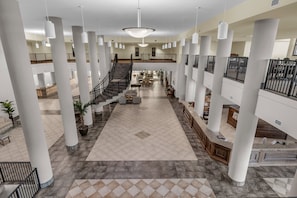 Un hall d’entrée spacieux avec de hauts plafonds, de grandes colonnes, un escalier central et une mezzanine.