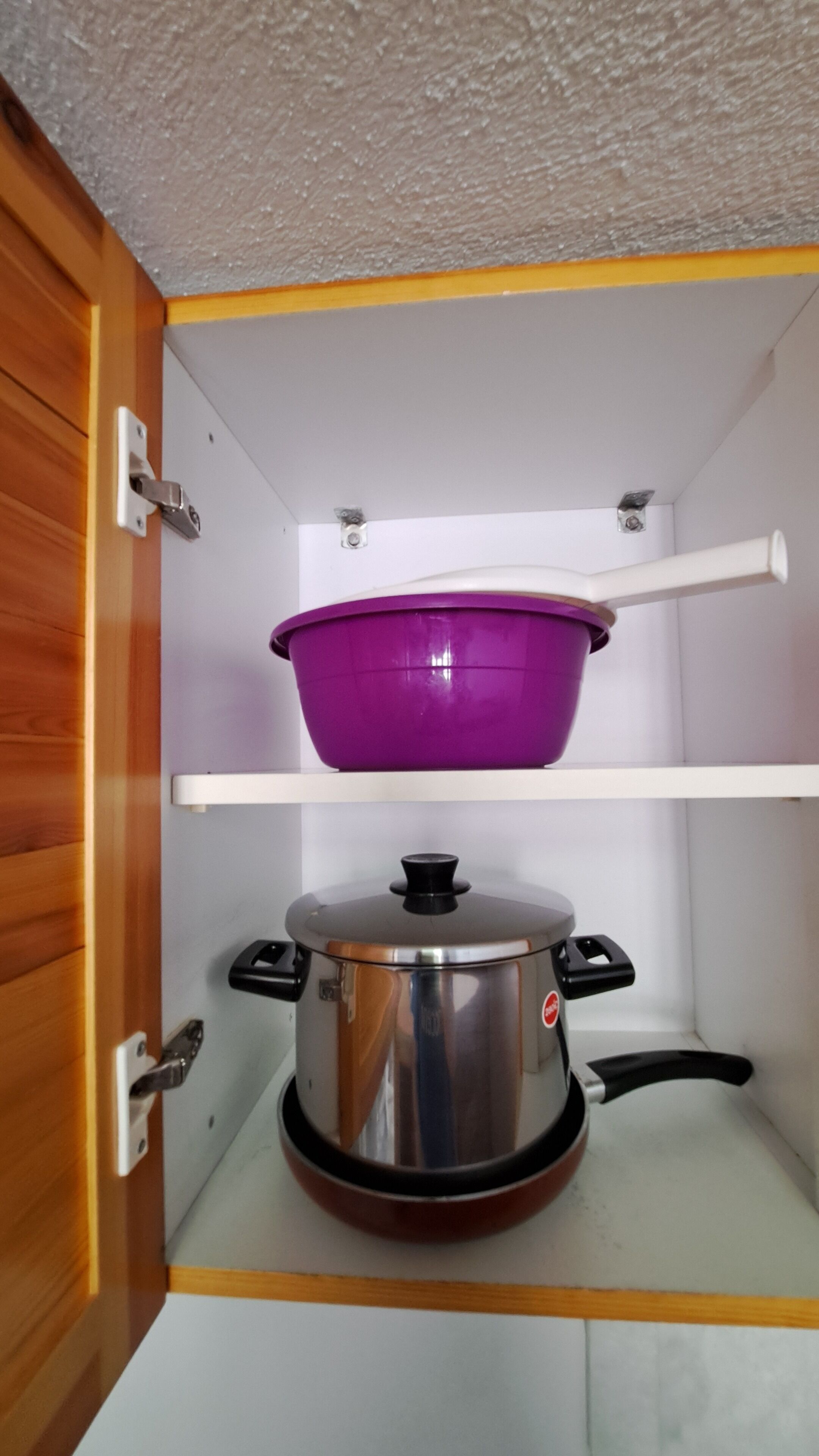 A kitchen cabinet with a purple pot on the top shelf and a stainless steel pot on the bottom shelf.