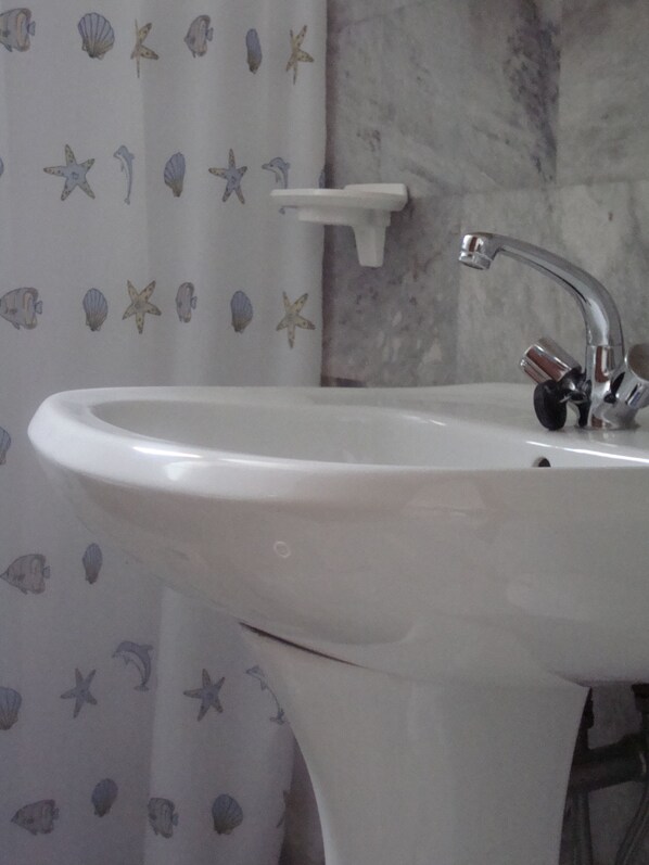 Une salle de bain avec un lavabo blanc, un miroir et un rideau de douche orné d’un motif sur le thème de la mer.