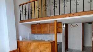 Een slaapkamer met een houten bed, een kleine kitchenette en een balkon met een hekwerk.