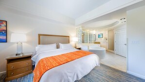 A hotel room with a large bed, a bedside table with a lamp, a bathroom with a bathtub, and a mirror. - 2 BR at Marriott Cypress Harbour (Orlando)