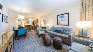 A hotel room with a living area, a dining table with chairs, a sofa with cushions, a coffee table, and a lamp. - 2 BR at Marriott Cypress Harbour (Orlando)