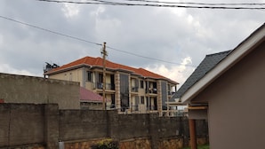 A two-story building with a red-tiled roof, a stone wall, and a paved driveway. - Tranquil Corner Kampala (Kampala)