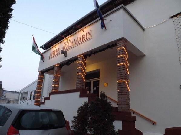 Hotel llamado "HOTEL AQUARIUM" con un letrero, pilares de ladrillo y un coche estacionado en la entrada.