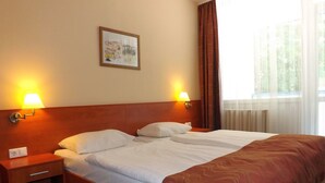 A hotel room with a double bed, two bedside lamps, a nightstand, a power outlet, and a window with curtains. - Aquamarin Hotel (Hévíz)