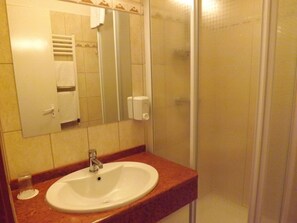 Un baño con lavamanos, espejo, dispensador de toallas y cabina de ducha de vidrio.